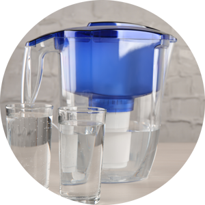 Filter jug and glasses with purified water on white table indoors.